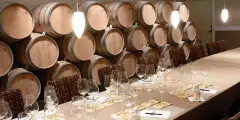 Seated tasting table with glasses in front of stacked wine barrels